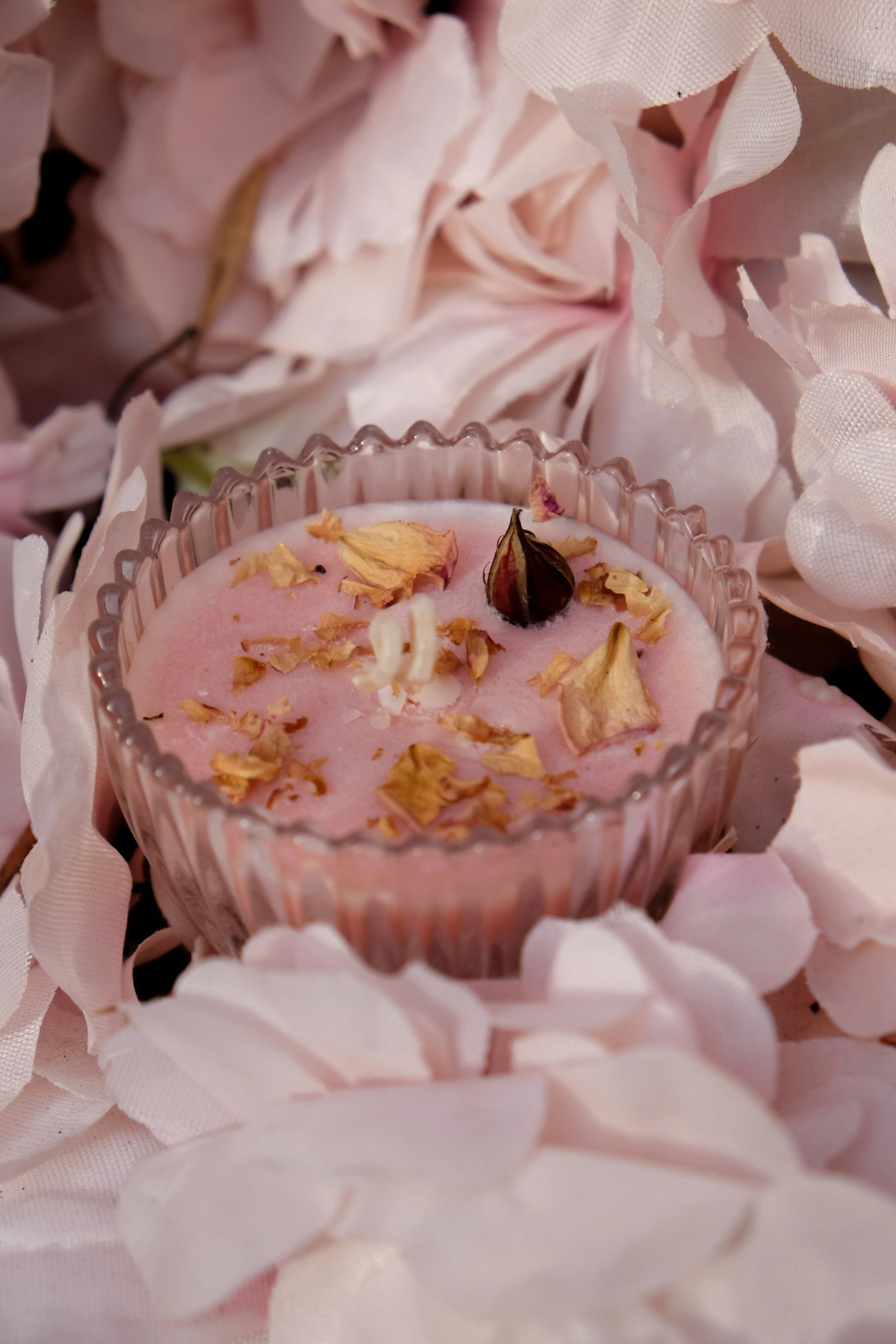 Bougie rose aux pétales de rose séchés dans une coupe en verre ciselé